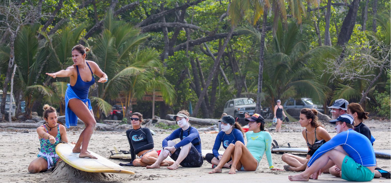 A surf instructor shows the pop-up on a board in the sand while students watch on Jacó beach, Costa Rica